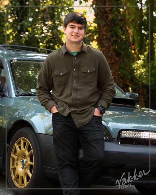 Ben Phelps' high school senior photo standing in front of his blue Subaru
