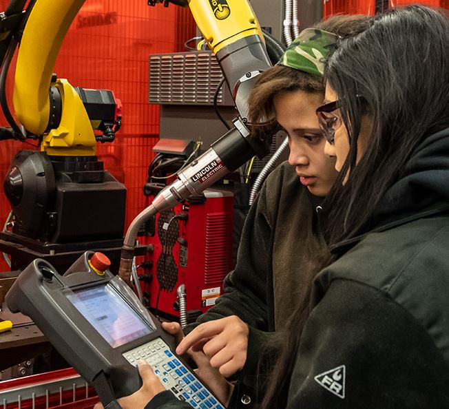 Two female welding students program the welding robot