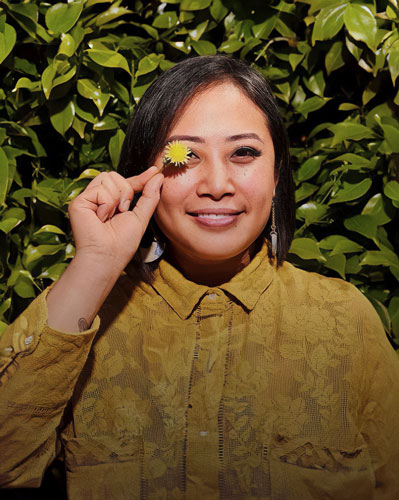 Chef Melissa Miranda smiling, holding a tiny sunflower over her right eye 