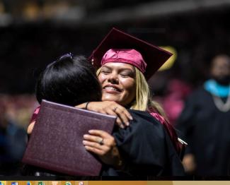 Female student hugs faculty member after receiving her diploma